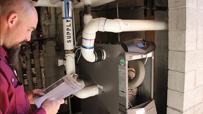Technician reviewing service paperwork while inspecting a residential boiler system