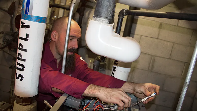 Technician adjusting wiring inside a residential boiler unit during heating system repair