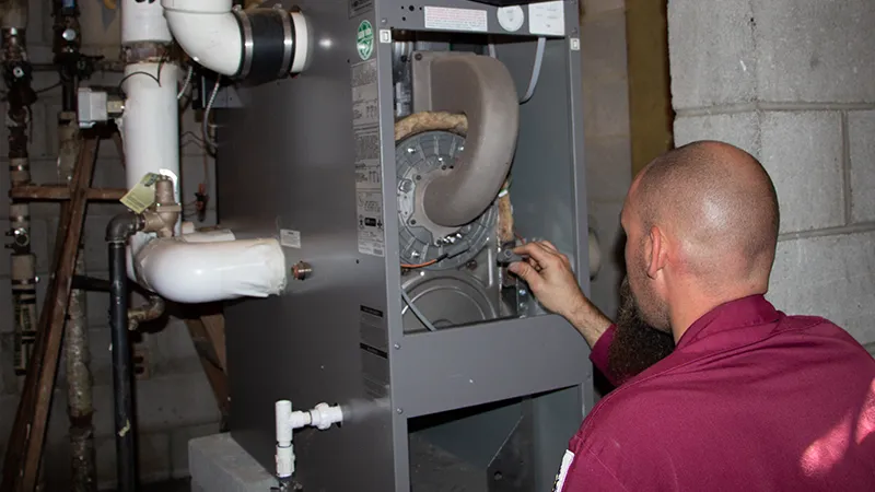 The technician is working on a residential boiler system in a basement.