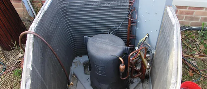 Outdoor air conditioning unit with the access panel removed, showing the compressor, condenser coil, wiring, and internal components.