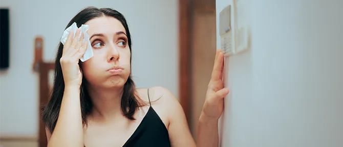 Woman feeling hot while adjusting a home thermostat.