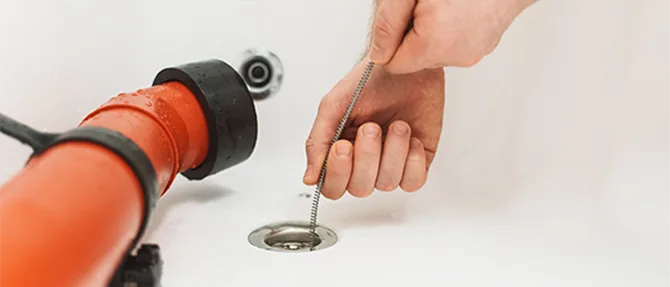 Plumber using a drain snake to clear a clogged bathroom sink drain.