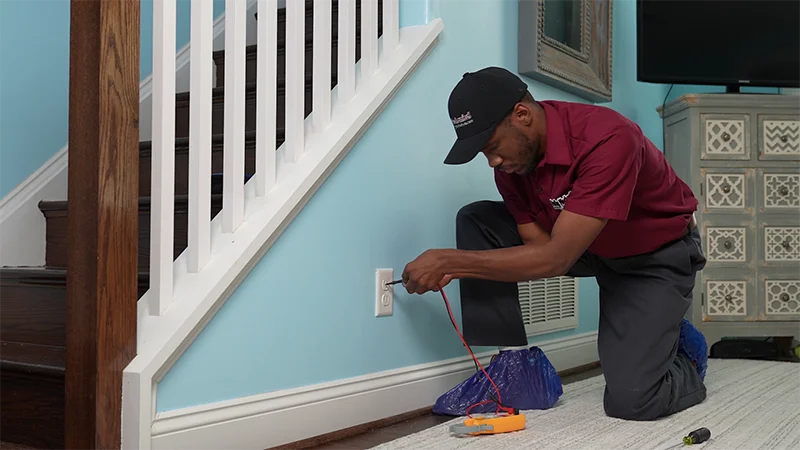 Professional electrician testing a wall outlet inside a home using electrical diagnostic equipment.