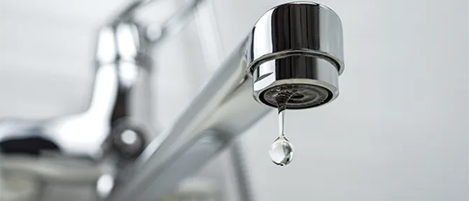 Close-up of leaking faucet with a water droplet forming at the spout.