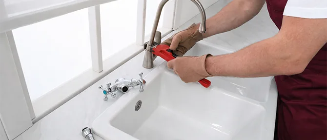 Plumber repairing a faucet with a wrench over a utility sink.