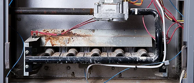 Close-up view of a furnace burner assembly showing rust buildup