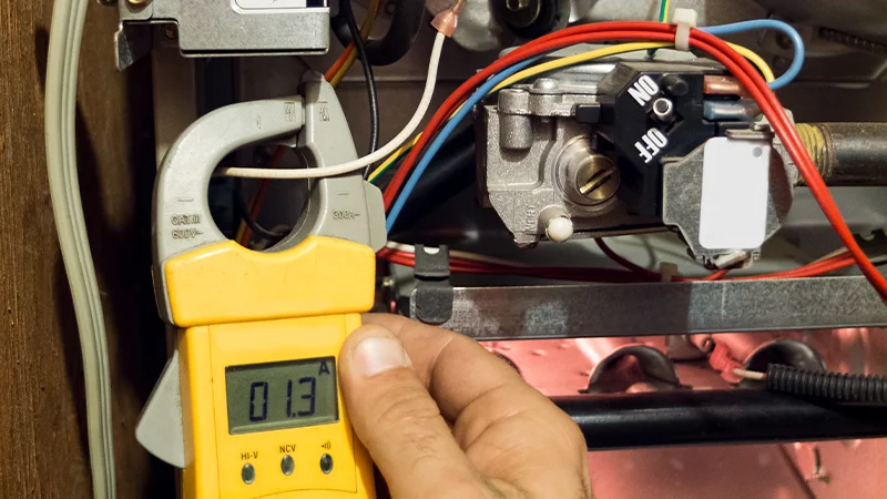 Technician measuring electrical current on a furnace component using a digital clamp meter
