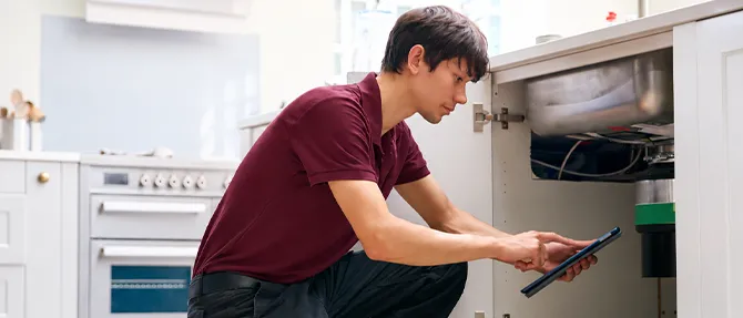 Technician using a tablet to inspect a garbage disposal under a kitchen sink.
