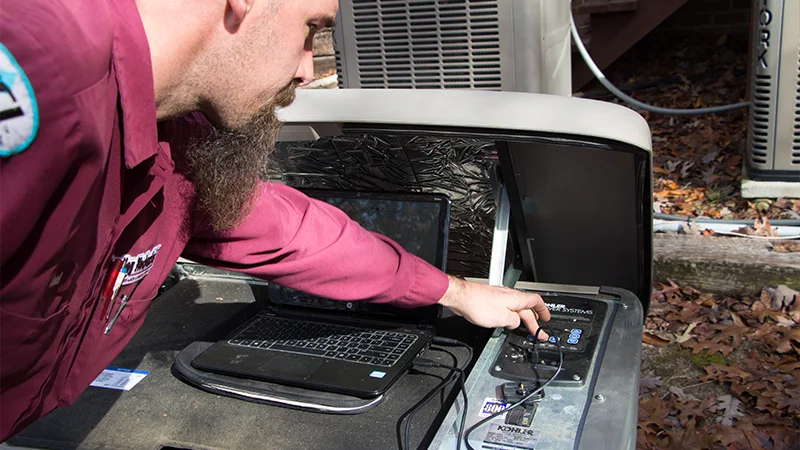 Technician testing a standby generator control panel using a laptop, with the generator housing open outdoors.
