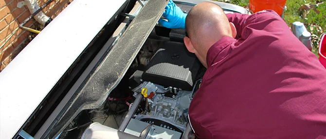 Technician performing maintenance on an open Generac standby generator, inspecting internal components beside a residential home.