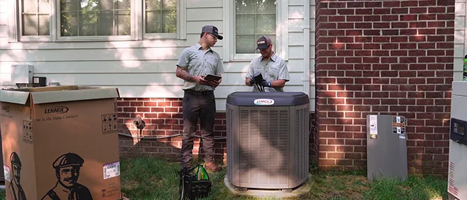 HVAC technicians installing a residential outdoor heat pump unit beside a brick home during professional heat pump installation