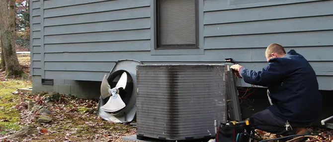 Technician performing maintenance on an outdoor heat pump unit near a home exterior