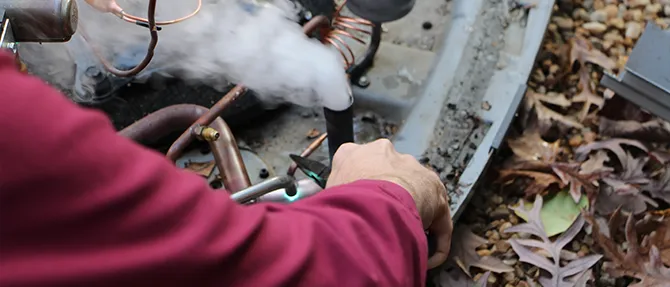 HVAC technician repairing heat pump with torch