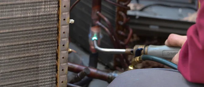 HVAC technician using a torch to repair copper lines near an outdoor condenser coil