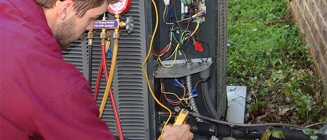 HVAC technician testing electrical connections and gauges while servicing an outdoor heat pump unit