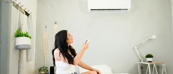 Homeowner using a remote control to adjust a wall-mounted ductless mini-split air conditioner.