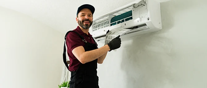 HVAC technician removing and inspecting the air filter from a wall-mounted ductless mini-split system during routine maintenance.