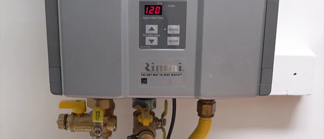 Close-up of a Rinnai propane tankless water heater displaying 120°F with visible gas line and water connections beneath the unit.