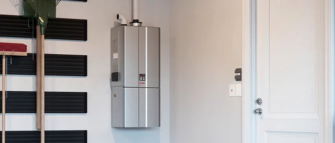 Wall-mounted tankless water heater installed in a residential garage next to storage shelves and a closed door.