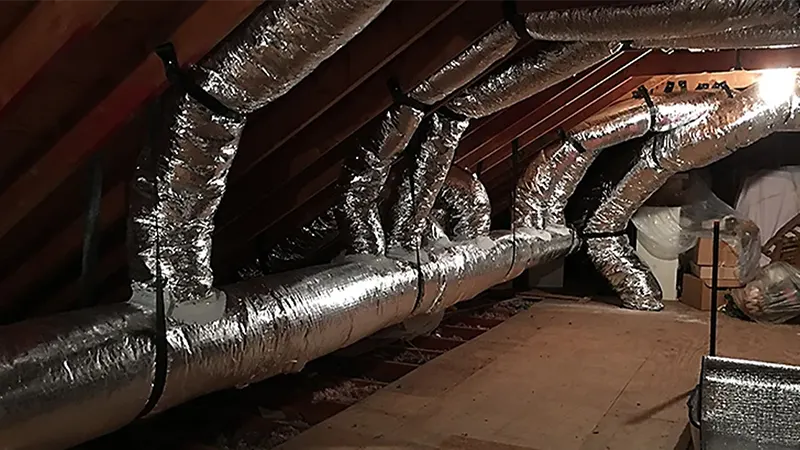 Insulated HVAC ductwork installed in an attic space with exposed wooden beams and flexible air ducts running throughout the ceiling.