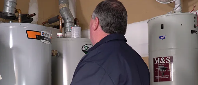 Technician inspecting residential water heaters and ventilation pipes in a utility room.