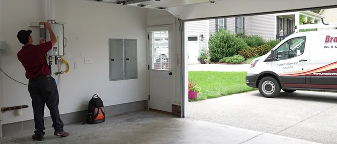 Technician installing or servicing a tankless water heater inside a residential garage with a service van parked outside.