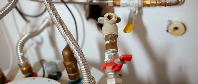 Detailed view of water heater plumbing system with valves, pipes, and flexible connectors